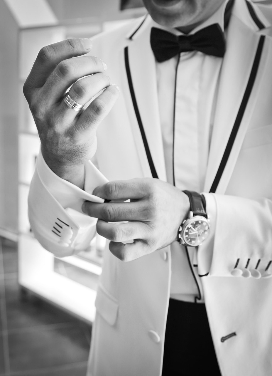 image shows man in white tuxedo with luxury goods